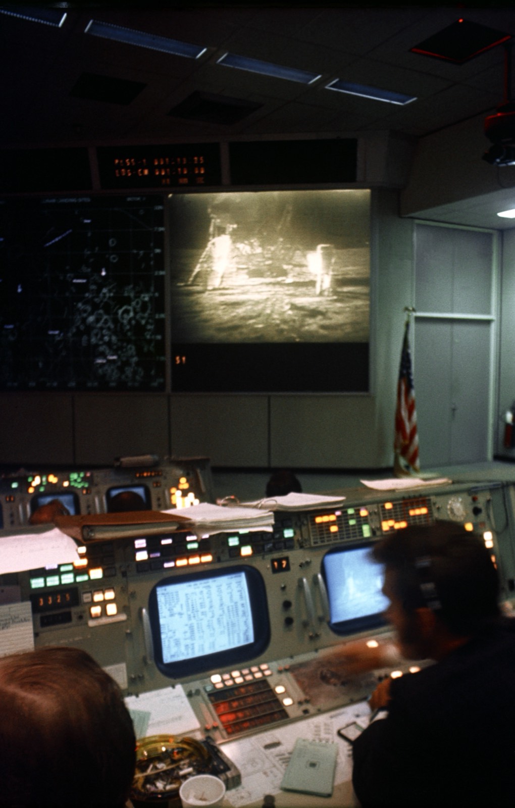 Apollo 11 mission control, consoles in the foreground and the moonwalk on the main screen