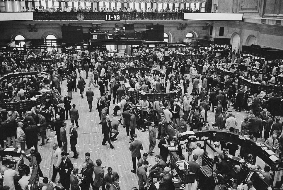 The floor of the New York Stock Exchange in 1961, seen from the gallery: hundreds of brokers and clerks working the horseshoe trading posts, order slips underfoot, the board clock reading 11:49